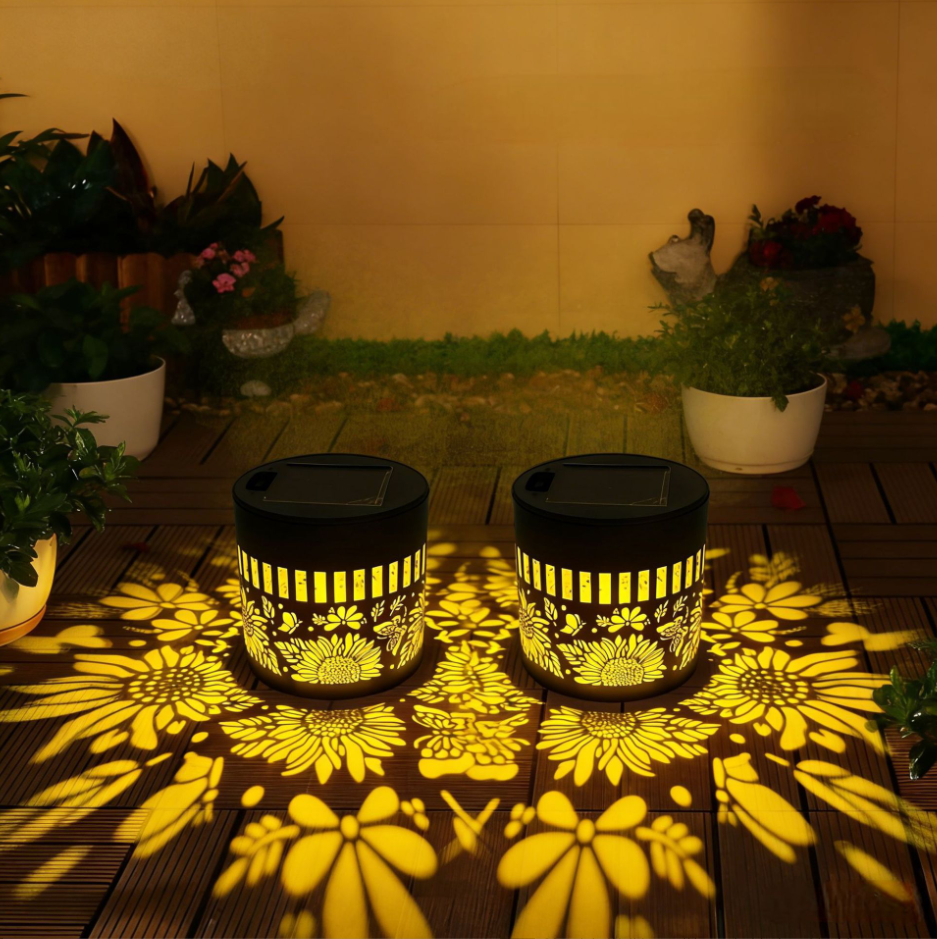 Două lămpi solare aprinse pe o terasă, cu proiecții de flori pe lemn